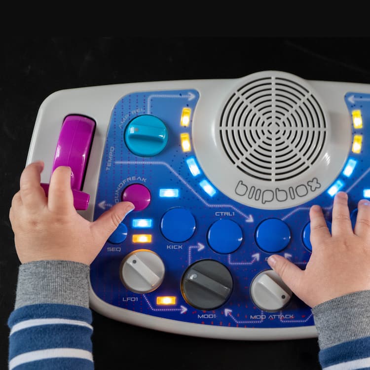 Baby's hands playing with a Blipblox SK2 on a black background