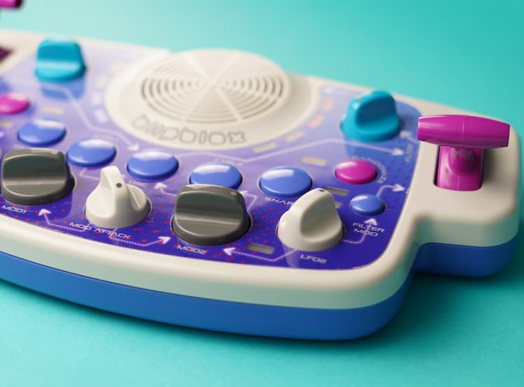 Detail shot of Blipblox SK2 showing colorful knobs, built-in speaker, buttons, and controls up close on a teal background.