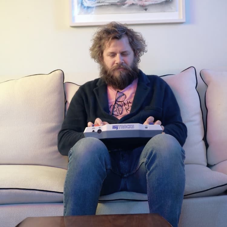 Man sitting on a couch holding Blipblox myTRACKS, wearing a black sweater and jeans.
