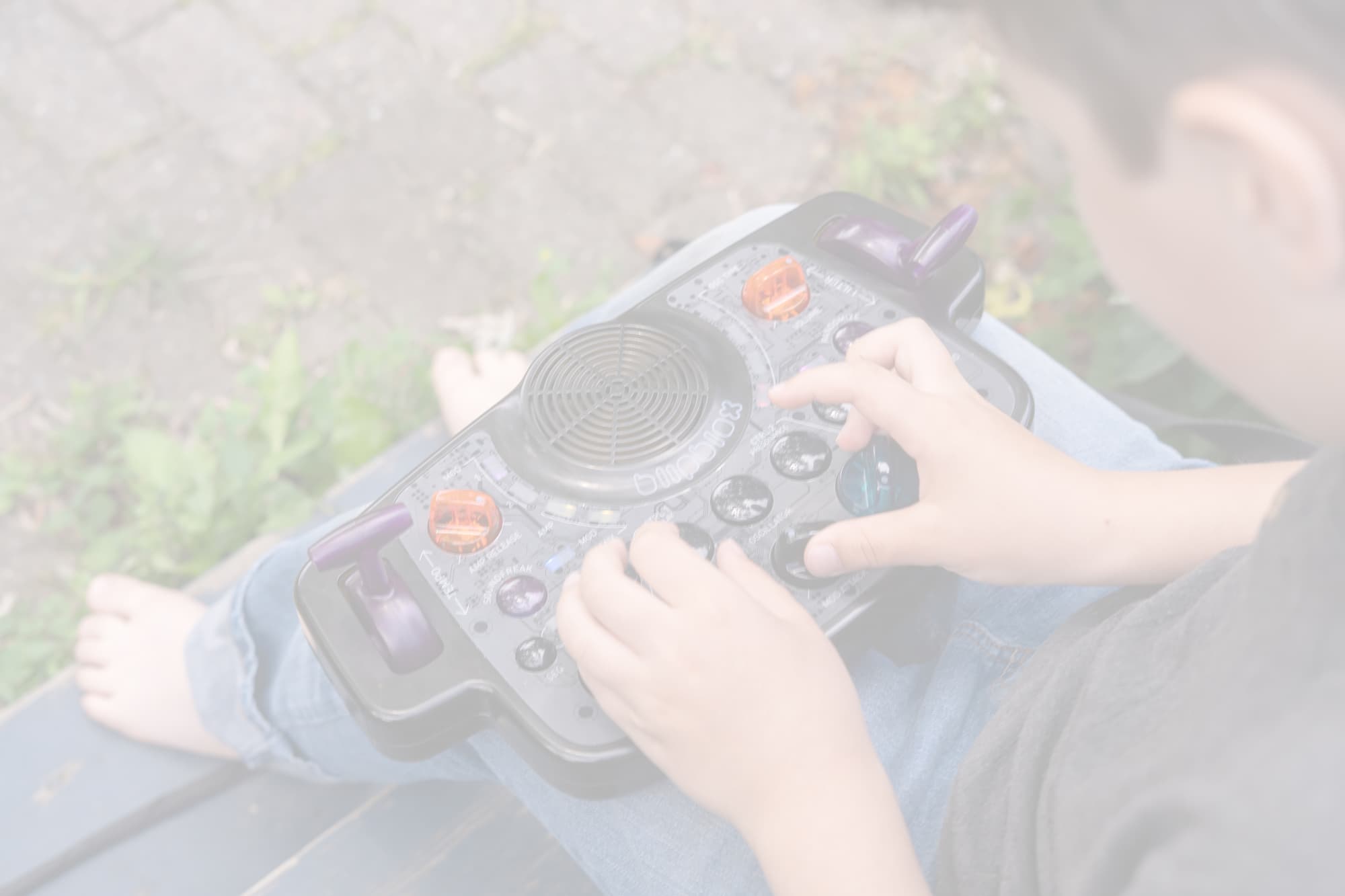 Kid exploring music with Blipblox After Dark portable synthesizer outside