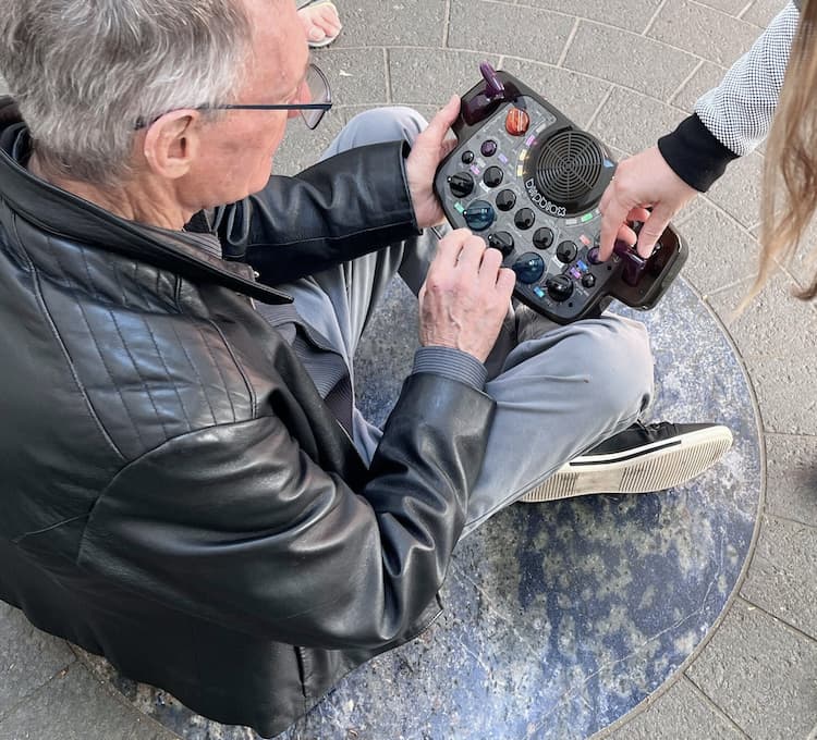 Older adult sitting on a stone patio using a Blipblox After Dark synthesizer.